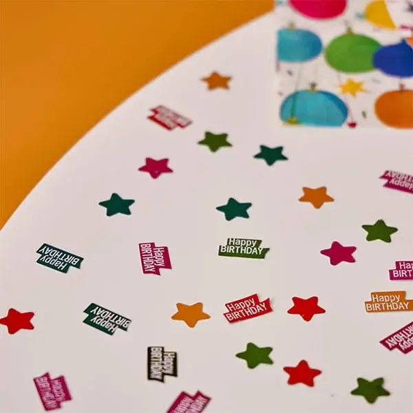 Colourful birthday table confetti with star shapes and Happy Birthday messages scattered across a party table.